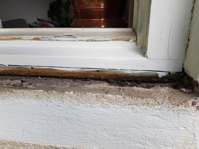 Skadad fönsterkarm och puts vid renovering som visar synlig trästruktur och sprickbildning.