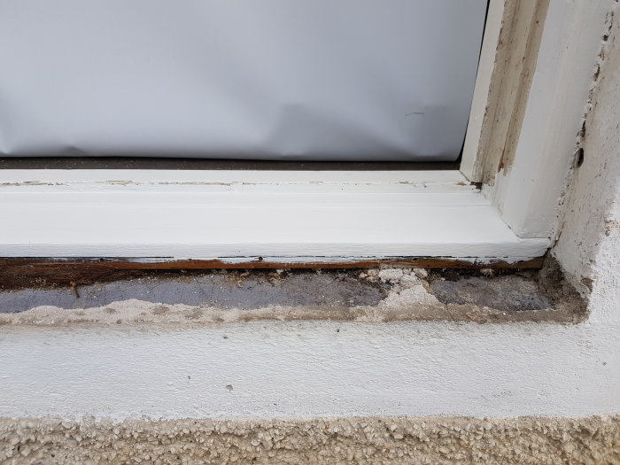 Närbild av ett renoverat fönster där putsen under fönsterblecket är skadad och har delvis avlägsnats.