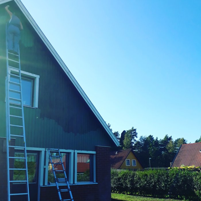 Ny målad gavel på ett hus med stege lutad mot väggen, under en klarblå himmel.