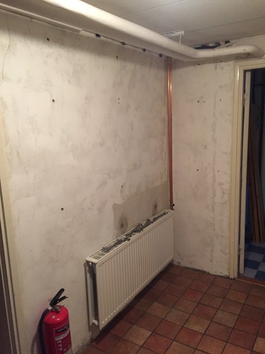 Nyinstallerad radiator med väl böjda kopparledningar på en omålad vägg i ett renoveringsprojekt.