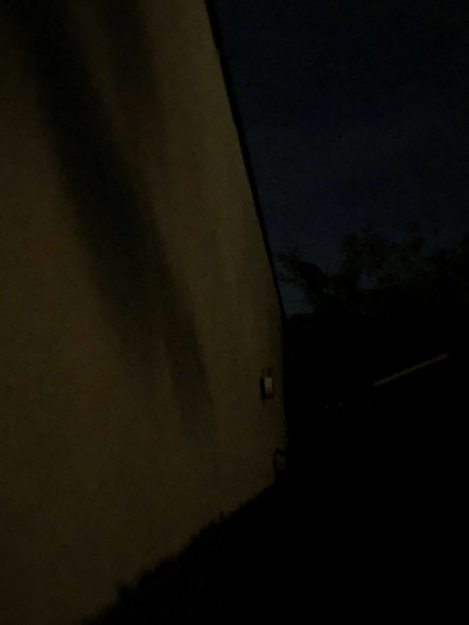 Mörk bild på en byggnads sida på kvällen med svagt synlig detalj som kan vara tempgivare.
