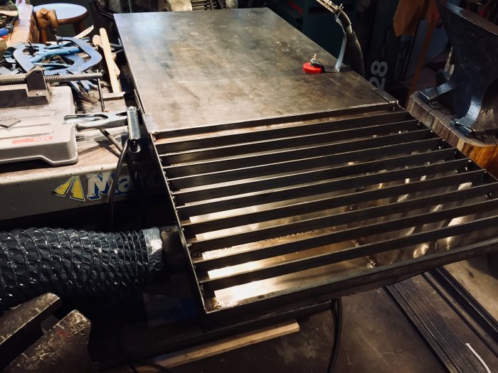 Downdraft-bord i verkstad med ansluten flexibel sugfläktsslang och rostfritt stos.