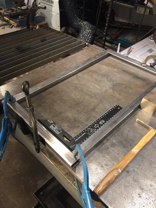 Metallverkstadsbild med downdraft-bord, sugfläktsslang och verktyg, för uppdatering av byggprojekt.