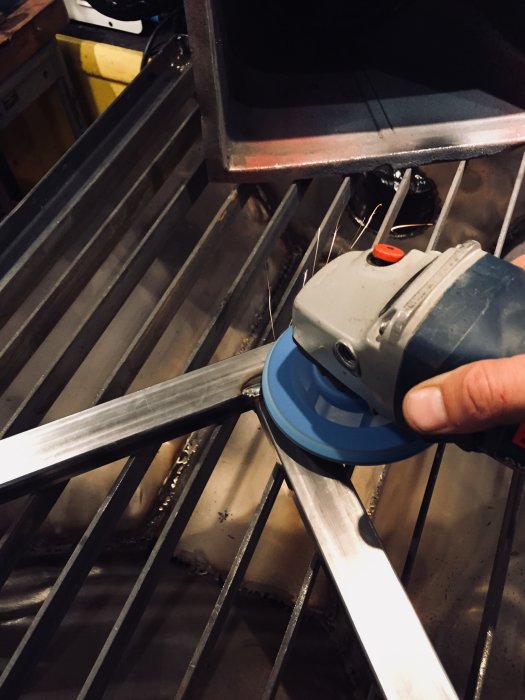 Handhållen slipmaskin som slipar kanten på en metallbit över ett metallgaller med sugfunktion.