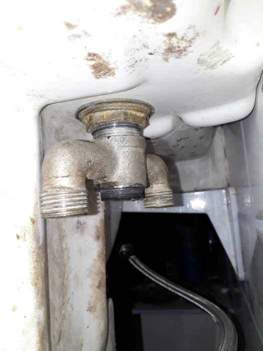 Gamla blandarens underdel med lossad låsring mot porslin, synligt godsrör och trångt utrymme.
