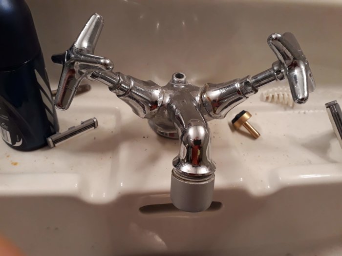 Gammal kromad blandare delvis demonterad, med lossade låsringar på ett handfat.