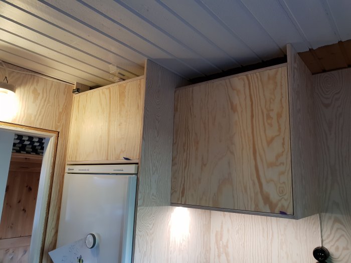 Kök med skåp klädda i plywood för ett enhetligt tema, plats för inbyggd belysning synlig vid det nedre hyllplanet.