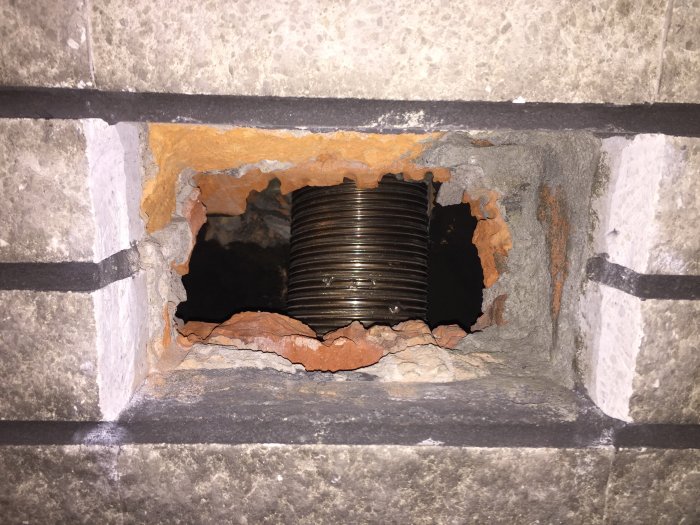 Ojämnt hål i skorsten med insatt metallgaller och synliga murade stenar med tjocka fogar.