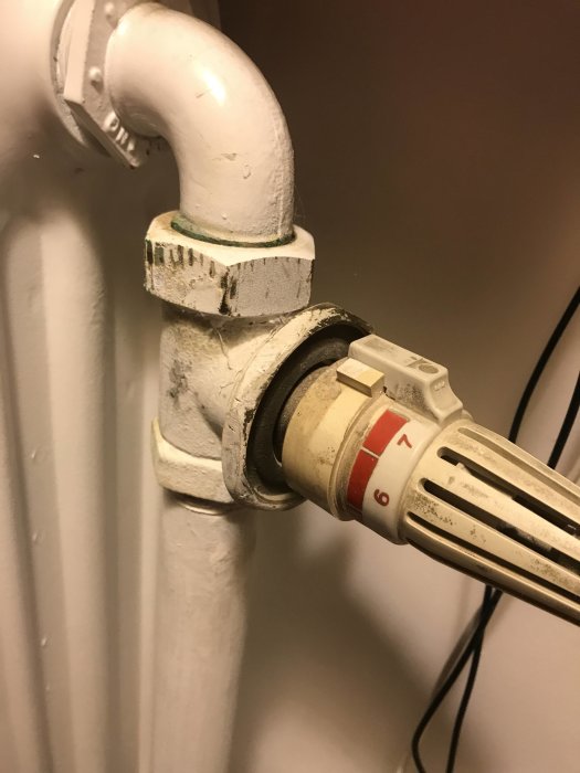 Radiatorkoppel och termostatventil i närbild på en vitmålad rörinstallation.