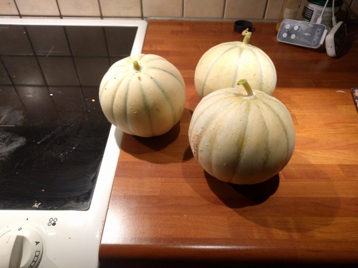 Tre mogna meloner på ett köksbänk bredvid en spishäll.