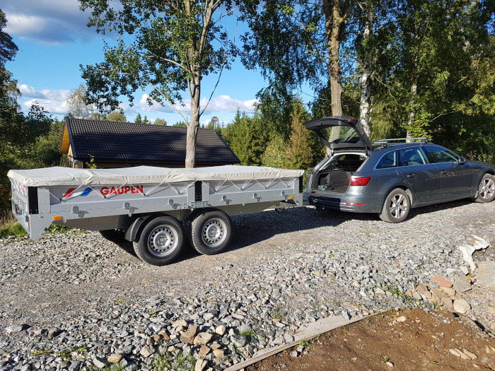 Gaupen E2635N släpvagn med grå presenning parkerad bredvid en grå Audi på en grusväg.