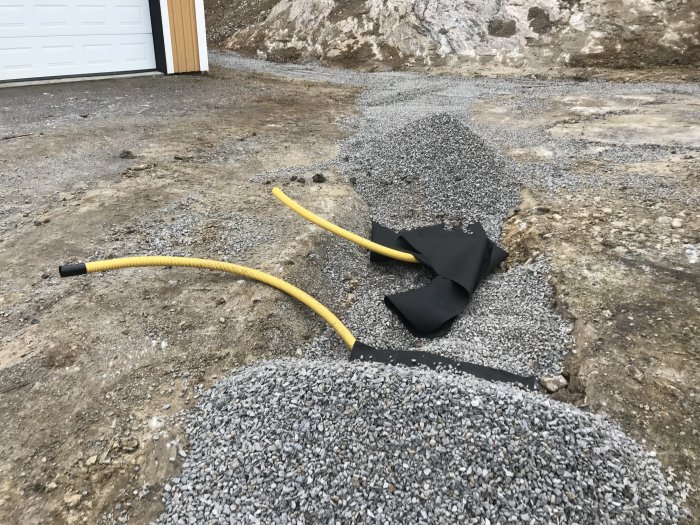 Gulrör för fiberoptisk kabel dras genom grusfylld grävd schakt på marken vid garage.