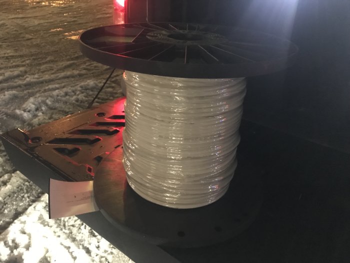 En rulle med fiberskyddsslang för husinstallation på en pall i snöigt landskap på kvällen.