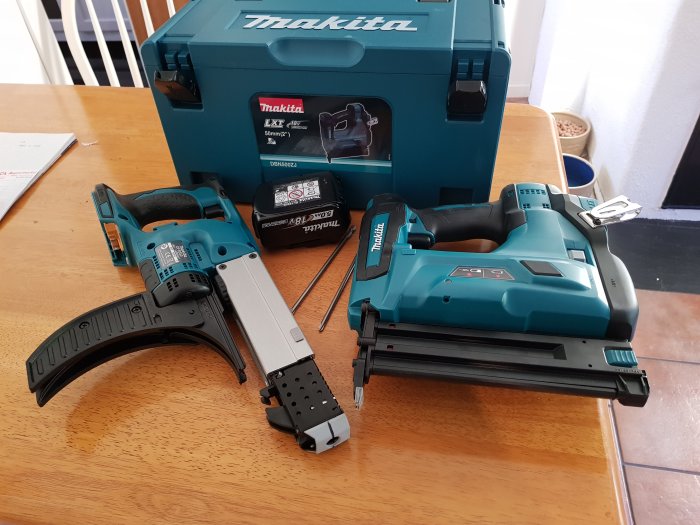 Makita verktyg inklusive skruvautomat DFR550, spikpistol DBN500ZJ och ett 5Ah batteri på bord med förvaringslåda.