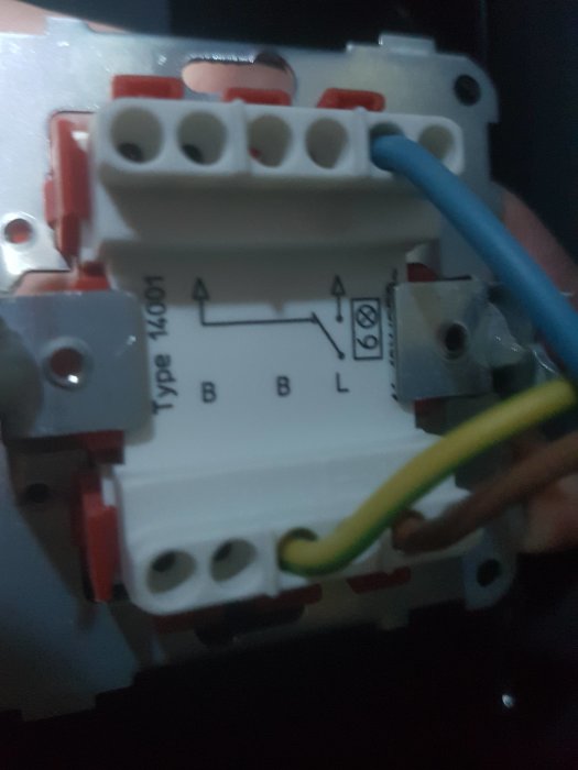 En hand som håller en ny strömbrytare med blå och gul kabel ansluten.