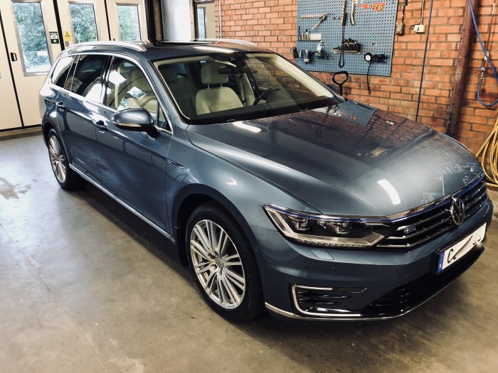 Blå Volkswagen Passat hybrid parkerad i ett garage med verktygstavla i bakgrunden.