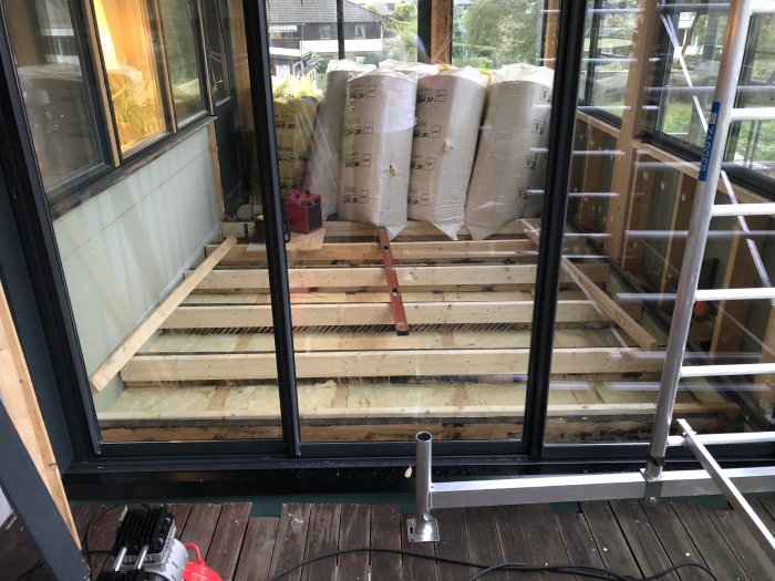 Riktat trägolv under konstruktion med isoleringsmaterial och byggsäckar i en glasad altan.