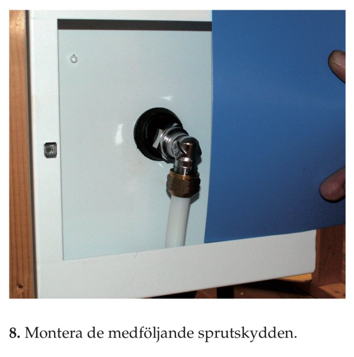 Installation av sprutskydd på en röranslutning i ett vitmålat skåp.