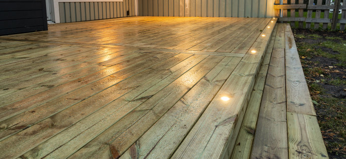 Nyligen byggd träterrass med inbyggda spotlights längs kanterna i skymningen, efter förbättringsarbete.