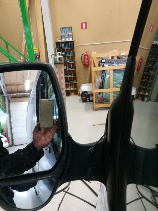 Person som håller en yttertemperaturmätare reflekterad i en bils sidospegel inuti ett garage.