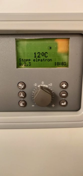 Termostat med display visande 12°C och olika kontrollknappar runt en central vred.