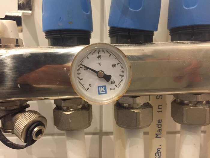 Termometer på rörsystem visar cirka 20 grader Celsius, omgiven av blå lock och ventilknoppar.