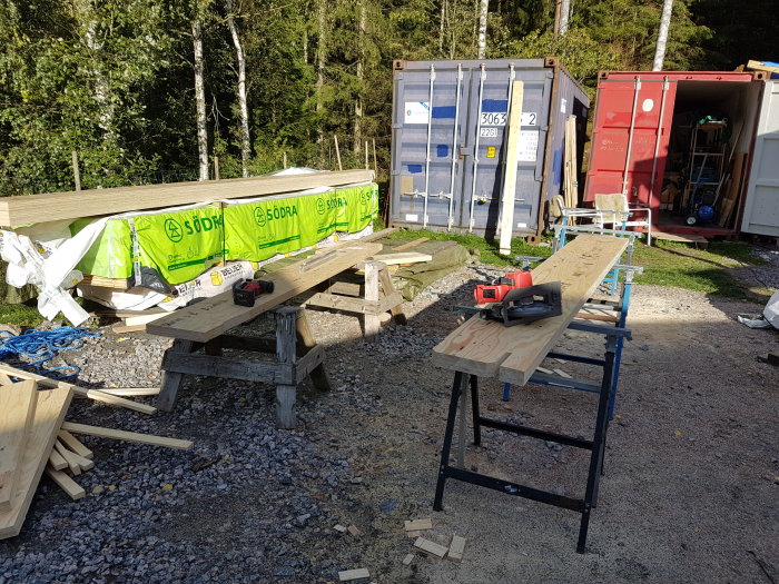 Kerto-balkar på sågbord utomhus, omgiven av byggmaterial och container.