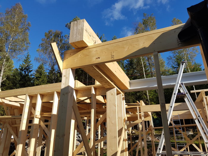 Nyssågade kerto-balkar monterade som bärande strukturer för en balkong, med väggstämpar och skogsbakgrund.