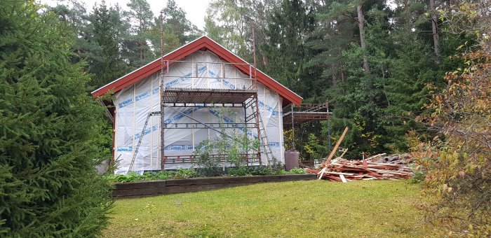 Hus under renovering med vindskyddspapp och byggnadsställningar, oisolerade paneler på marken.