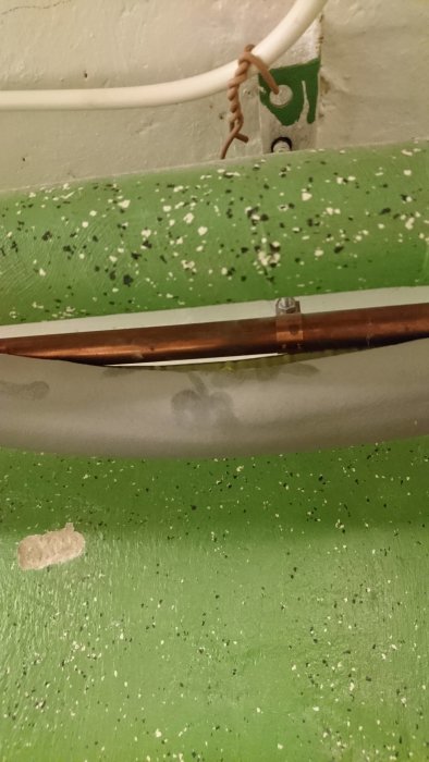 Kopparledning som passerar genom en isolerad vägg med fästen och eventuell asbestinnehållande böj.