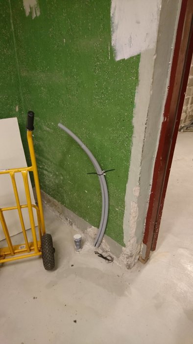 Grått flexibelt PEX-rör fäst längs en grön betongvägg i källare för VVS-arbete.