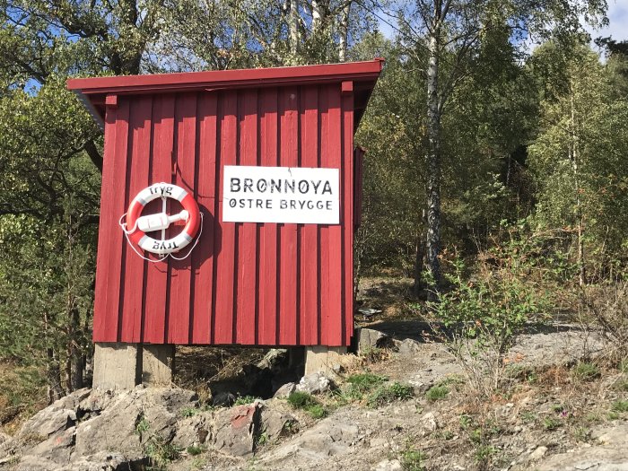 Rödmålat enkelt trähus vid vatten, tänkt att byggas om till bastu, med livboj och skylt "Brønnøya østre brygge".