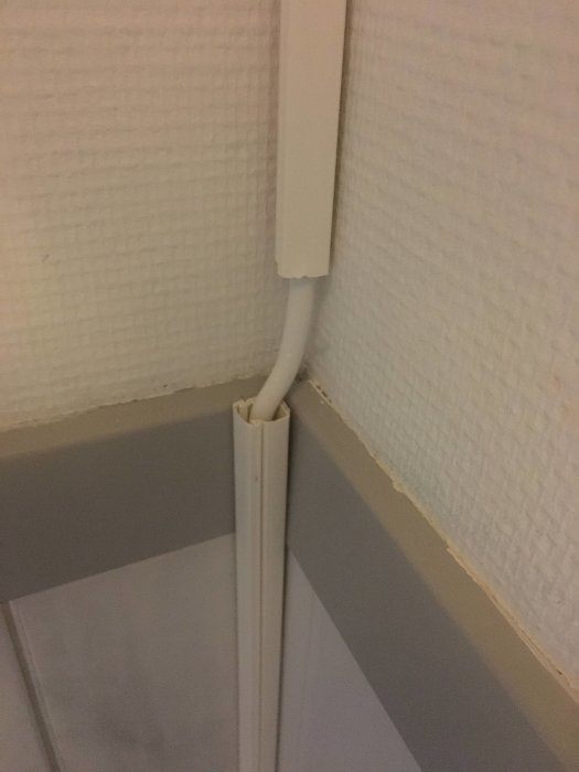 Kabelkanal i hörn med synlig kabel som böjer över en list.