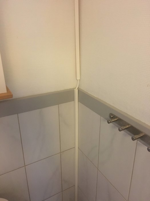 Elkanaldragning längs med en hörna där den går från golvet upp till taket ovanför kaklad vägg och trälist.