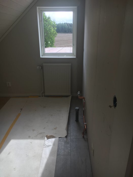 Kök under renovering med omonterade skåp och rörarbete, skyddspapp på golvet och fönster med utsikt.