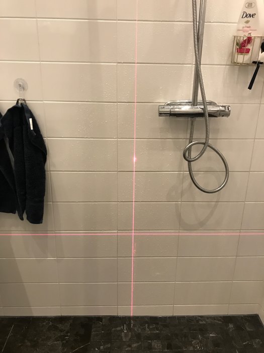 Duschkabin med kakelväggar och golv, markerade med en laserlinje för att visa ojämnheter och dåligt utförd fogning.