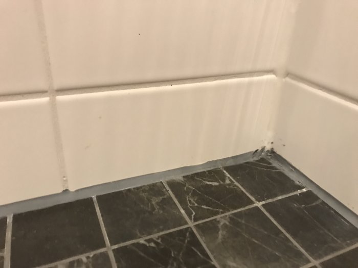 Ojämn och kladdig mjukfog mellan golvkakel och väggkakel i ett badrum.