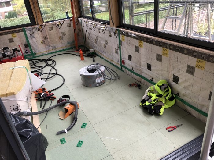 Ett uterum under renovering med nyisolerade väggar och verktyg utspridda på golvet.