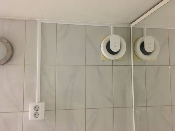 Elektrisk installation i våtrum med vägguttag och två infällda taklampor på kaklad vägg.