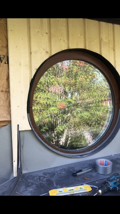 Runt fönster under installation med verktyg och nivå på en täckt arbetsyta, omgiven av ny panelvägg.