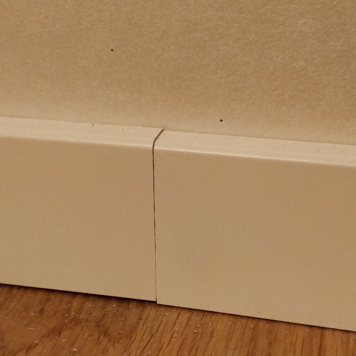 Otillräckligt justerad fogning mellan två vita golvsocklar.