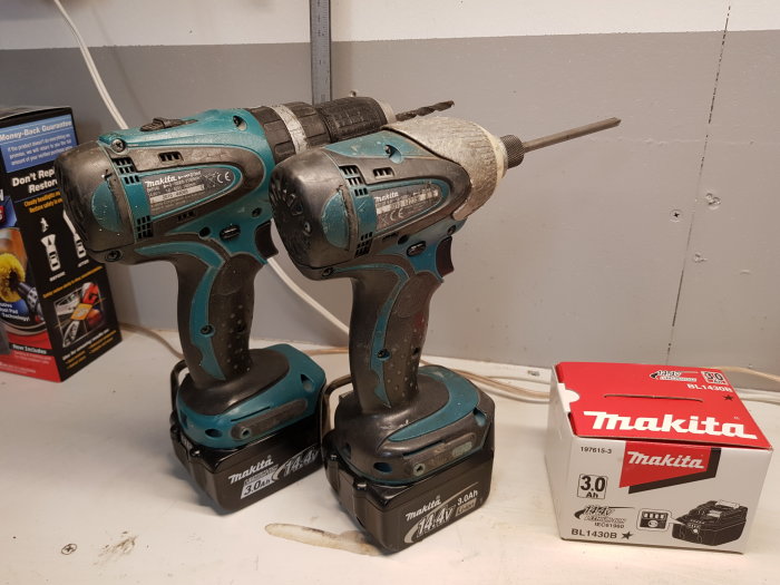 Två använda Makita skruvdragare och en ny Makita batteriförpackning på en arbetsbänk.