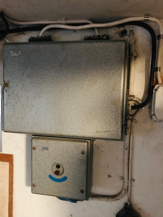 Gammal elektrisk undercentral och normcentral på en källarvägg med synliga kablar och rörinstallationer.