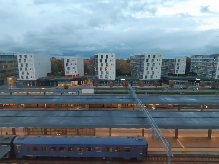 Kvällsutsikt över tågspår med förbipasserande tåg och moderna bostadsbyggnader.