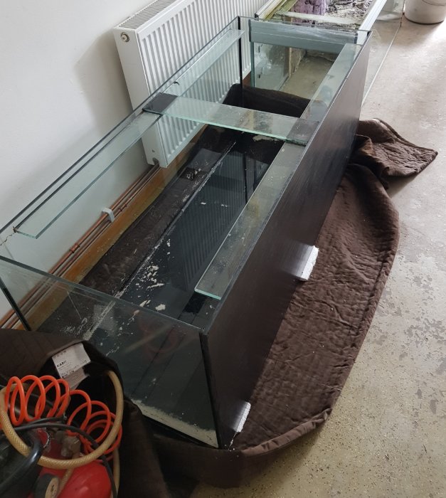 Tomt akvarium på 150x60x60 cm står på ett brunt tyg i ett garage.