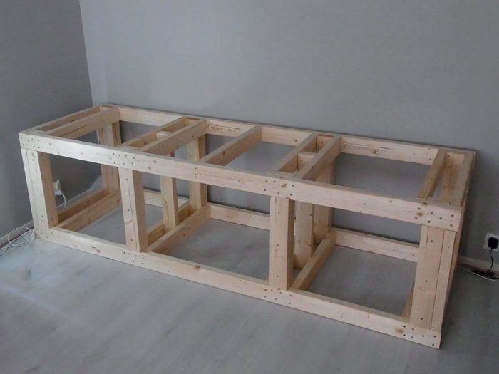 Träram för akvariebänk av virke utan beklädnad i ett grått rum.