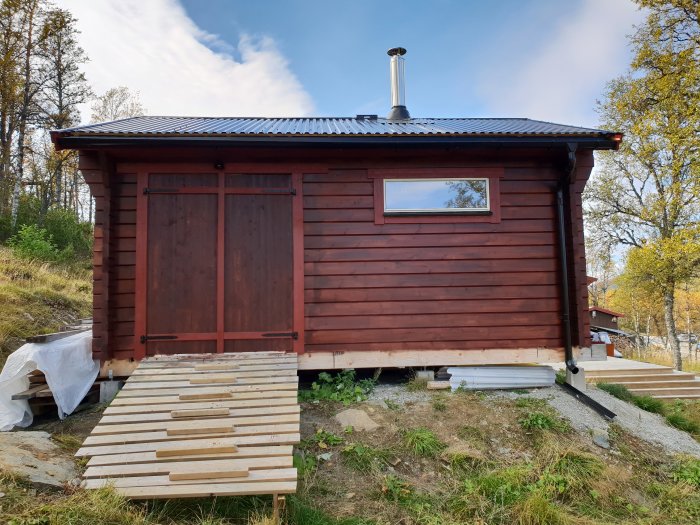 Nymålad röd stuga med tillhörande trädäck, trappa och skoterramp under klar himmel.