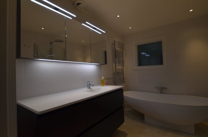 Modernt badrum med spotlights ovanför spegel och vid tak, fristående badkar och handdukstork.