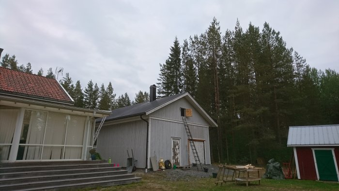 Ny skorsten på ett grått hus med vit veranda och skogslandskap i bakgrunden.