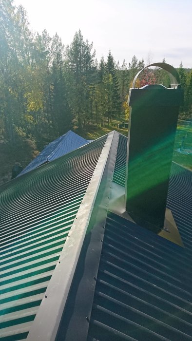 Nyligen installerad skorsten på ett plåttak med träd i bakgrunden.